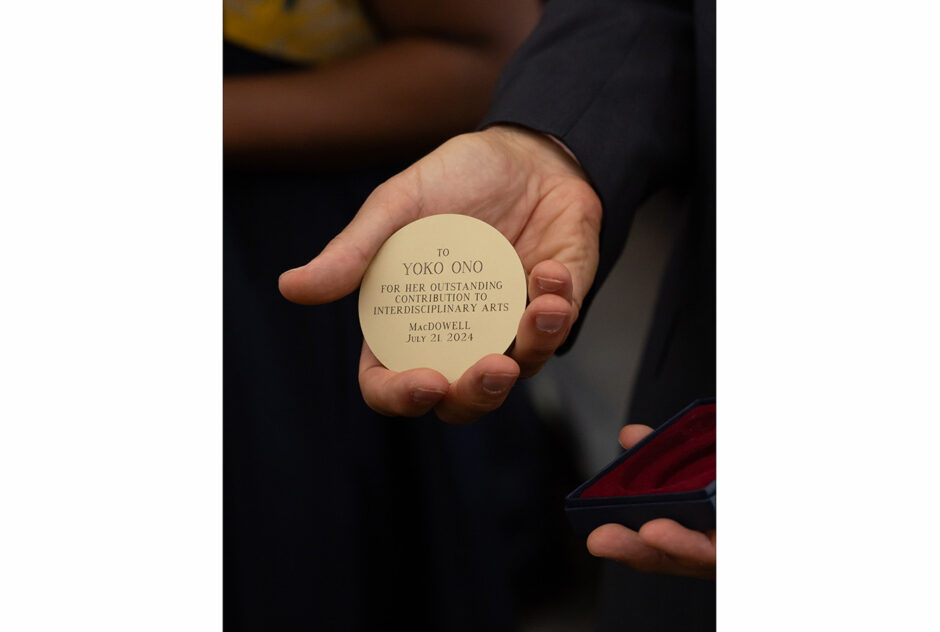 A closeup on a hand holding the Edward MacDowell Medal, a large brass coin.