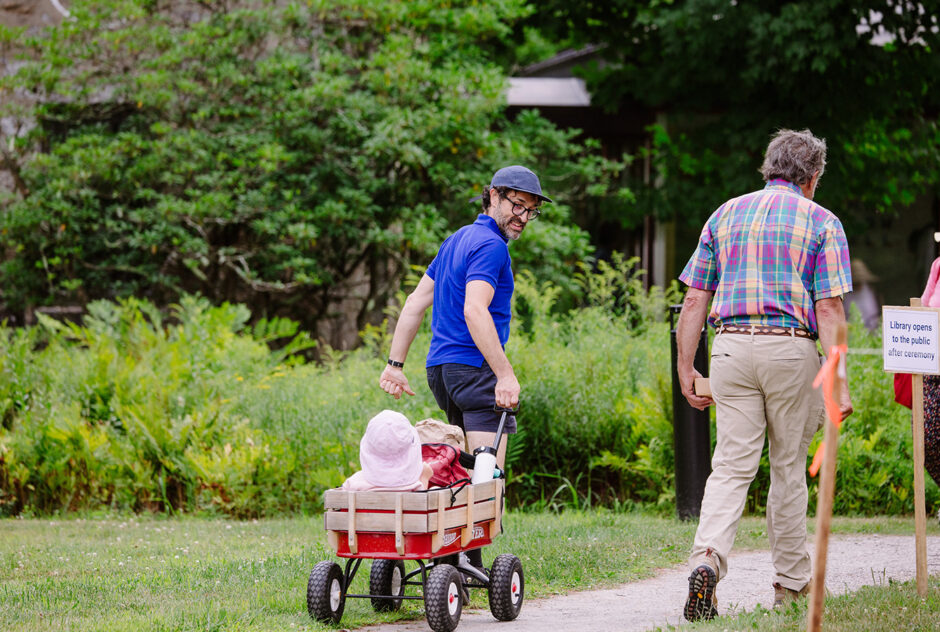 A man pulls a small child in a red wagon along a path. He looks back and smiles