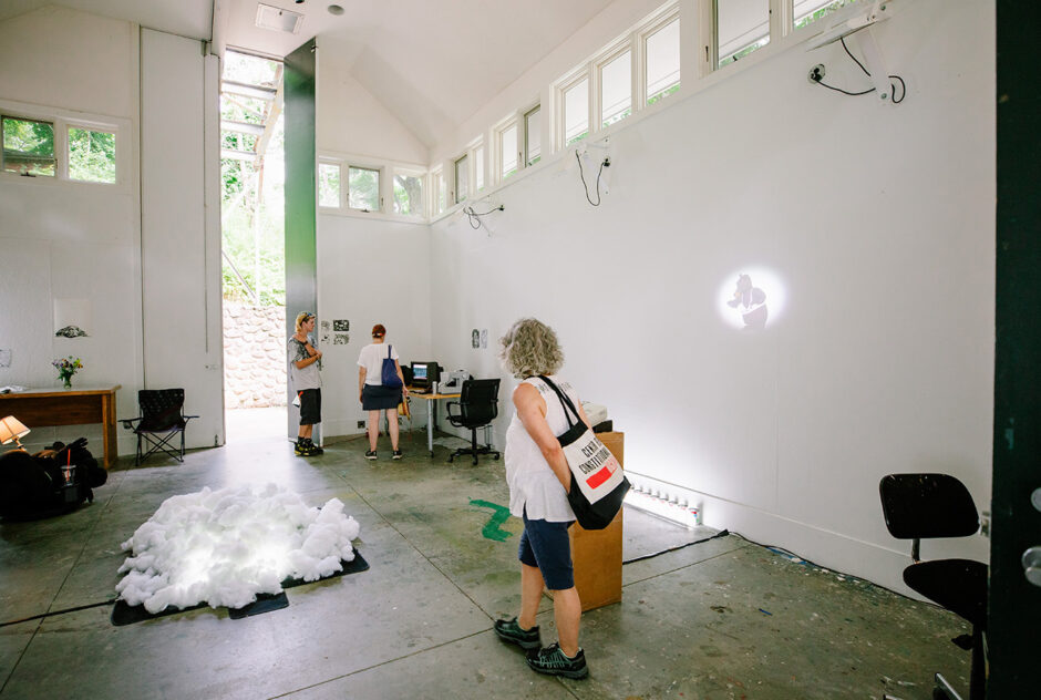 Three people, scattered around a large room, admire artworks that have been installed throughout the space.