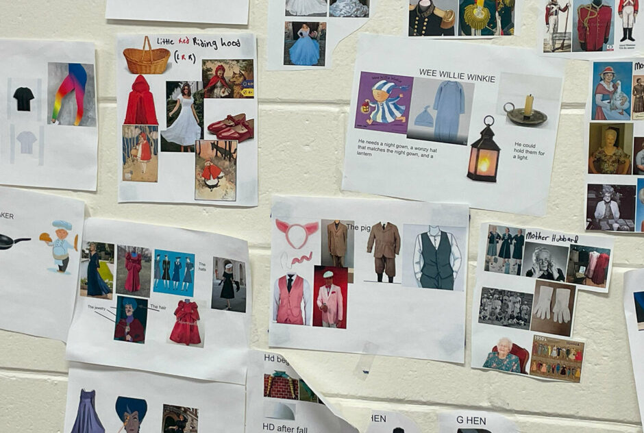 A white cinderblock wall adorned with pieces of paper. Each paper hosts the name, and costume ideas for characters in a play.