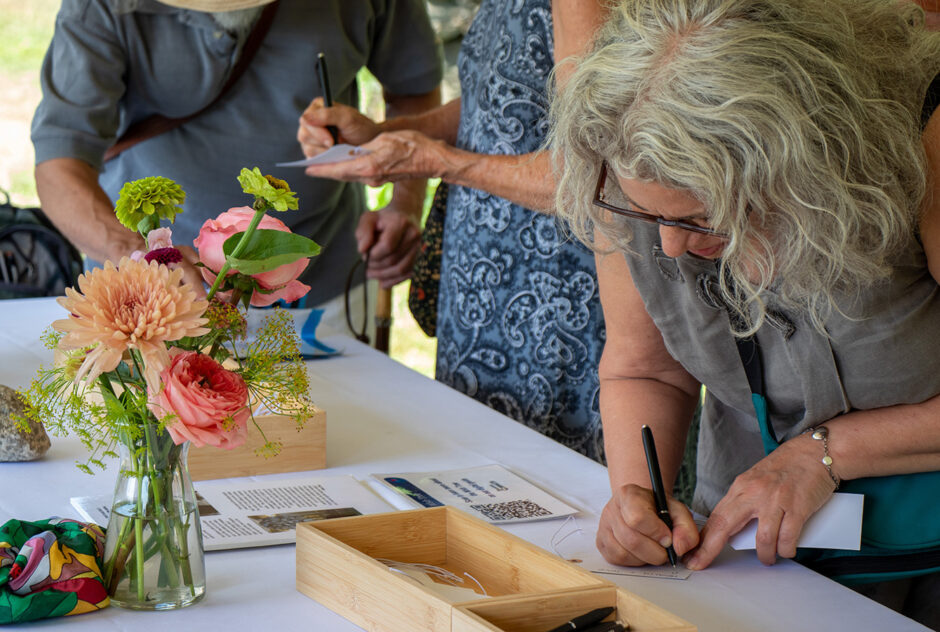 Three people gather around a table adorned with flowers and a white table cloth. They are writing on small pieces of paper.