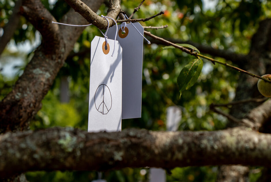 A small white tag hangs from the branches of a tree. On the tag, a peace symbol is written