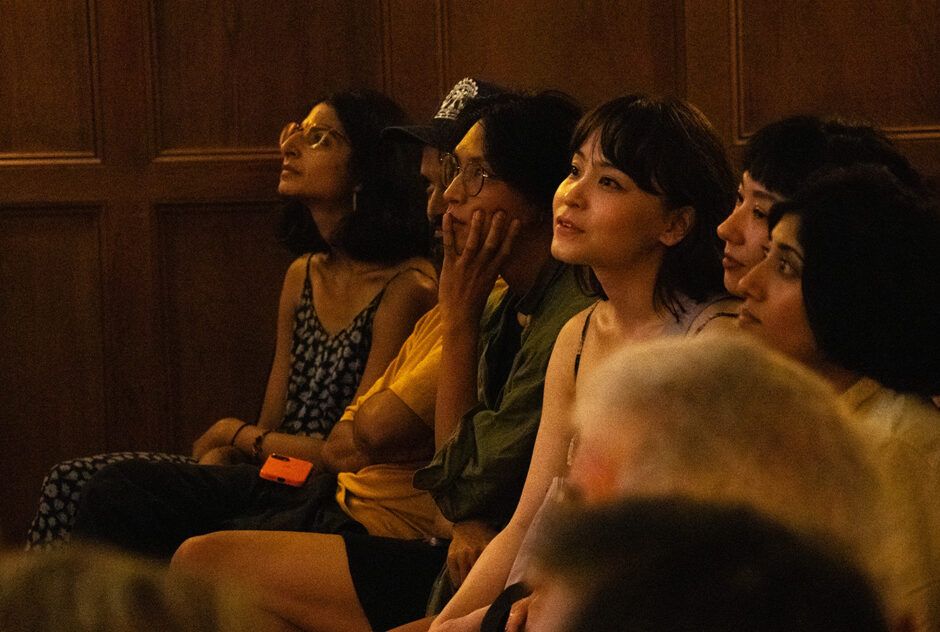 A row of people sit in chairs, looking toward the front of the room. They each have looks of concentration on their faces