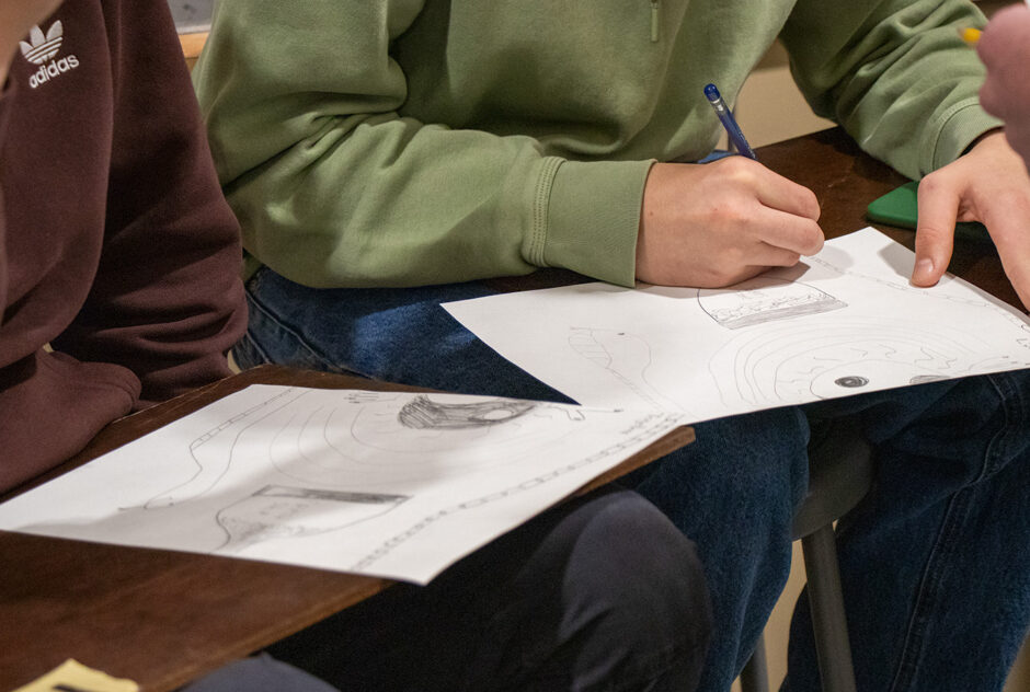 A close-up shot of two students who are sitting on stools. They are making a drawing together.