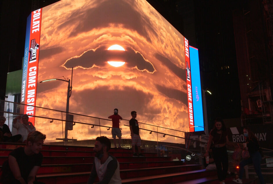 On a large billboard screen at a city street corner at night, video art (Kambui Olujimi's "In Your Absence the Skies Are All the Same") is projected for passersby and onlookers.