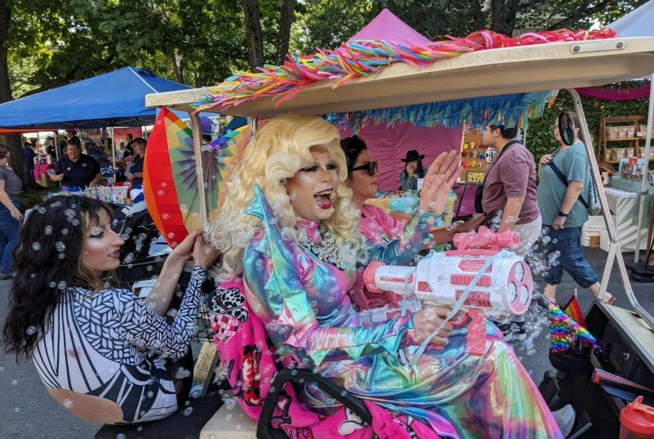 A golf cart with three immaculately dressed drag queens shoot bubbles from a bubble gun as they cruise around the festival