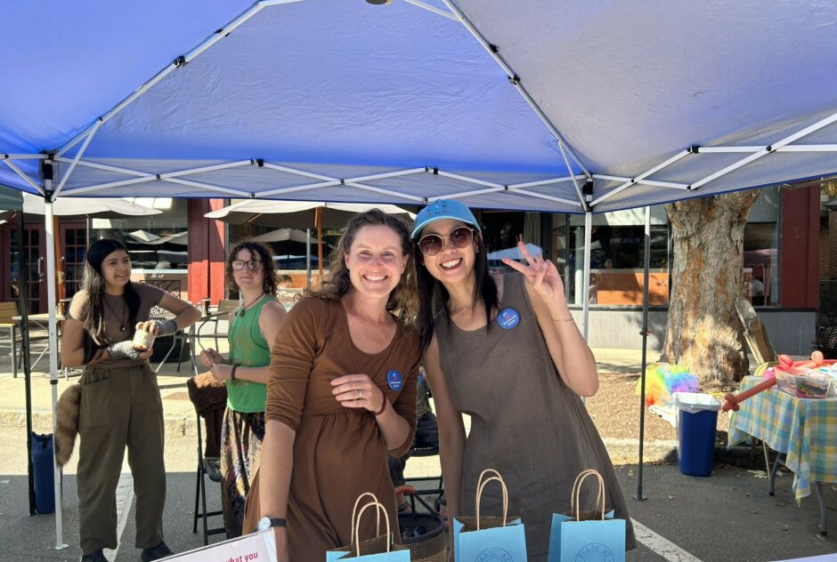 Two people pose for a picture while running a booth at a street festival