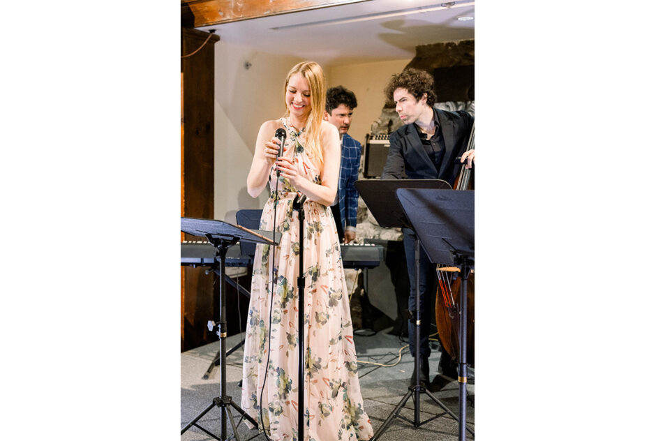 A woman in a pink long dress stands in front of a microphone that she is adjusting