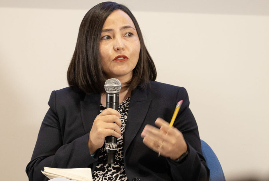 A female identifying person (Zahra Nader) talks and holds a mic while sitting.