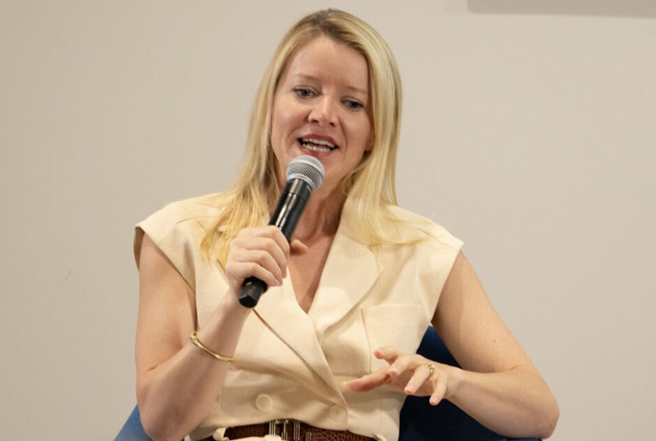 A female identifying person (Jane Ferguson) talks and holds a mic while sitting.