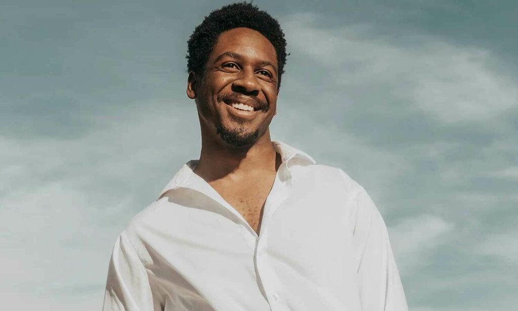 Kyle Rivera smiling broadly in a white shirt in full sun with sky behind him