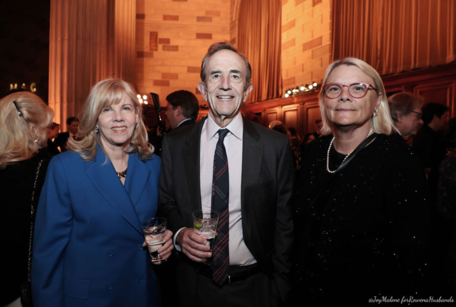 Three people wearing formal wear at a party smile and pose for a photo together