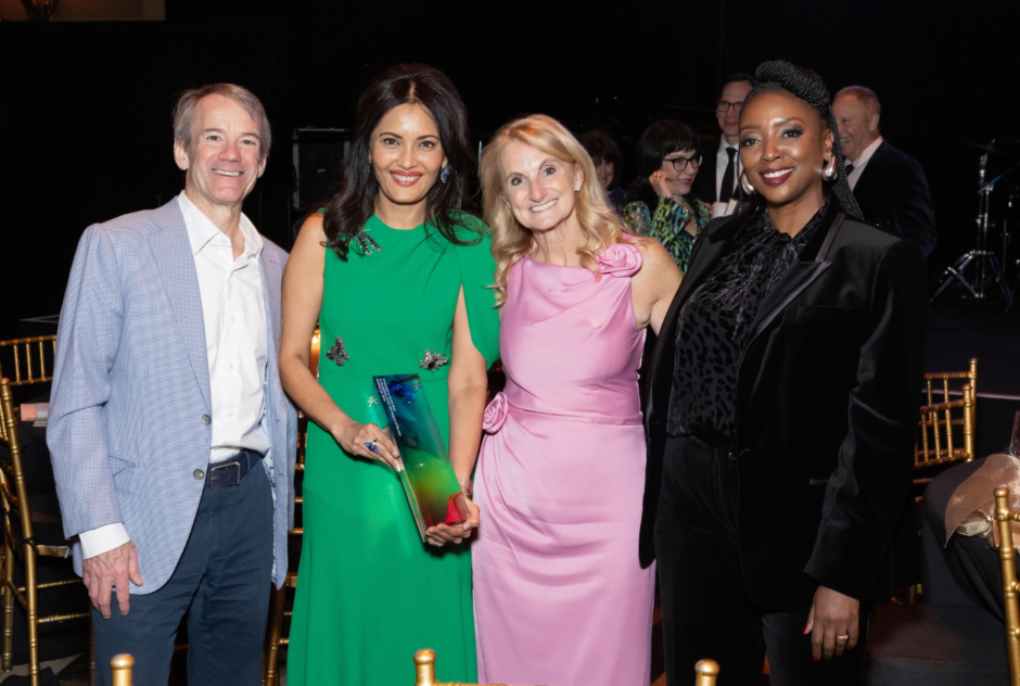 A group of people in colorful formal wear pose for a photo with a colorful glass award