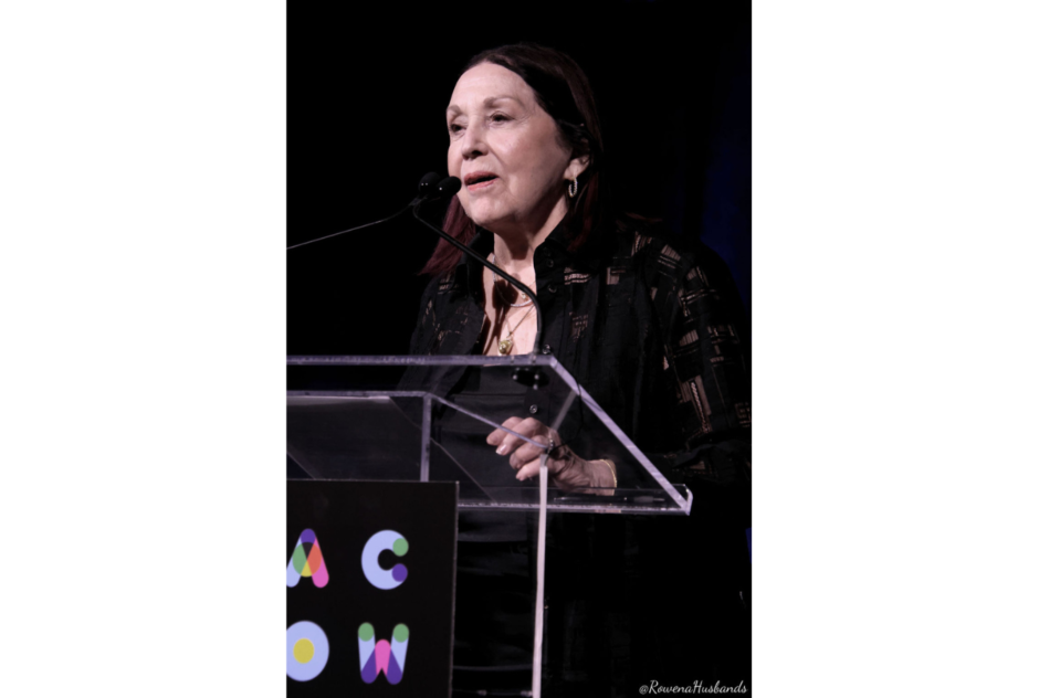 An older woman with dark hair speaks at a podium