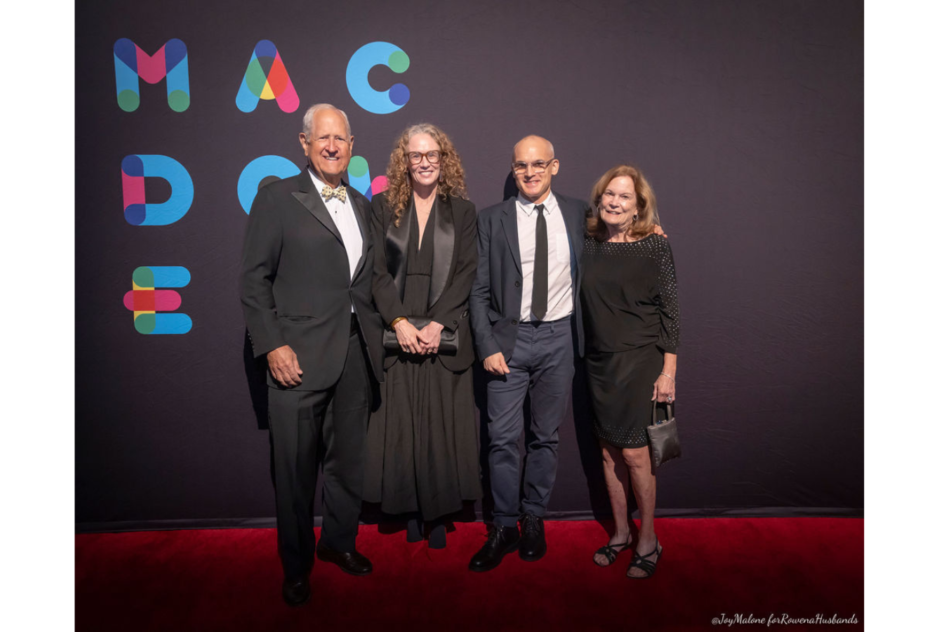 A group of people in formal wear smile in front of a black branded step and repeat