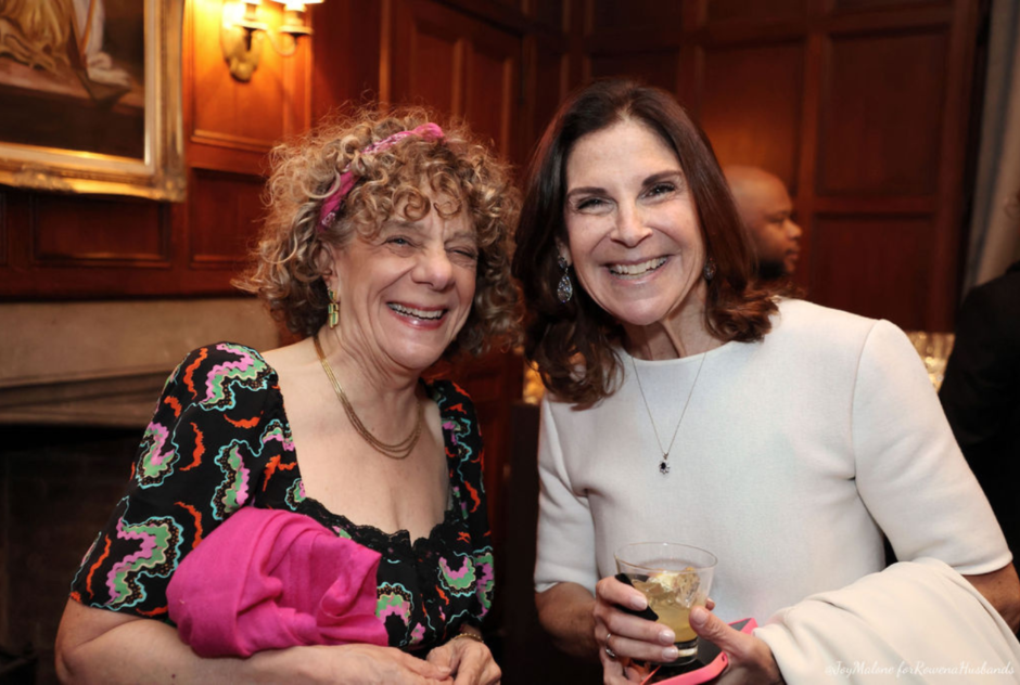 Two white woman wearing dresses smile in a close up photo at a party