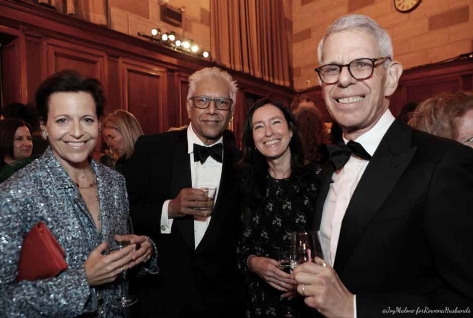 A group of guests wearing formal wear smile for a photo at a party with drinks in their hands