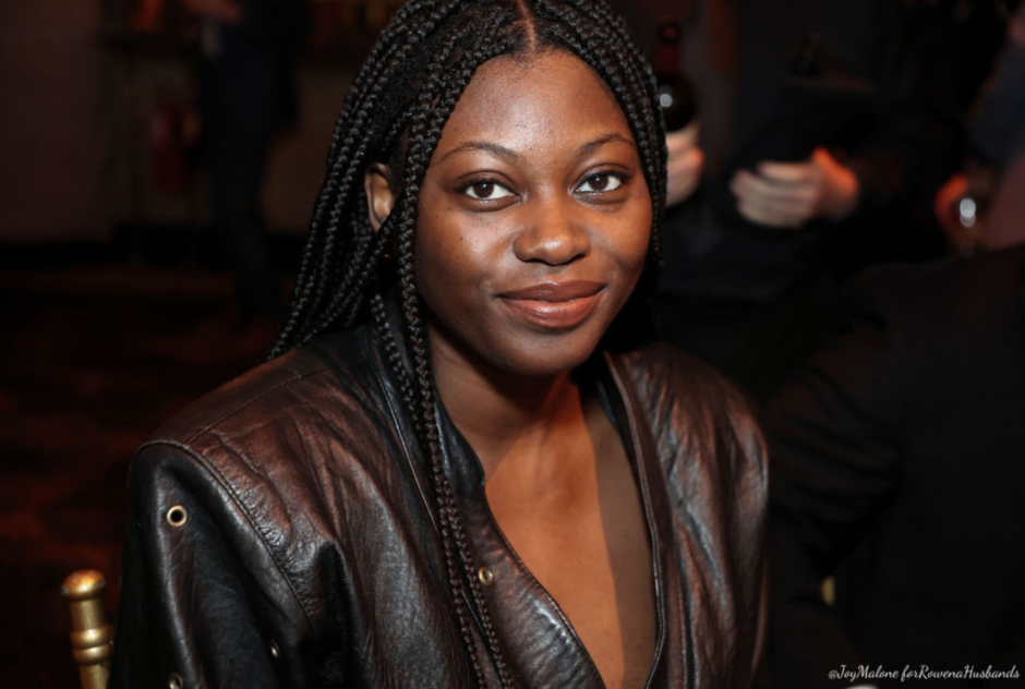 A woman in a dark brown leather jacket smiles at the camera in a close up