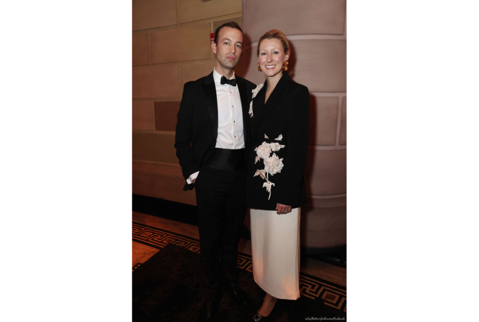 A man in a tuxedo and a woman in a formal two-piece outfit smile for a photo