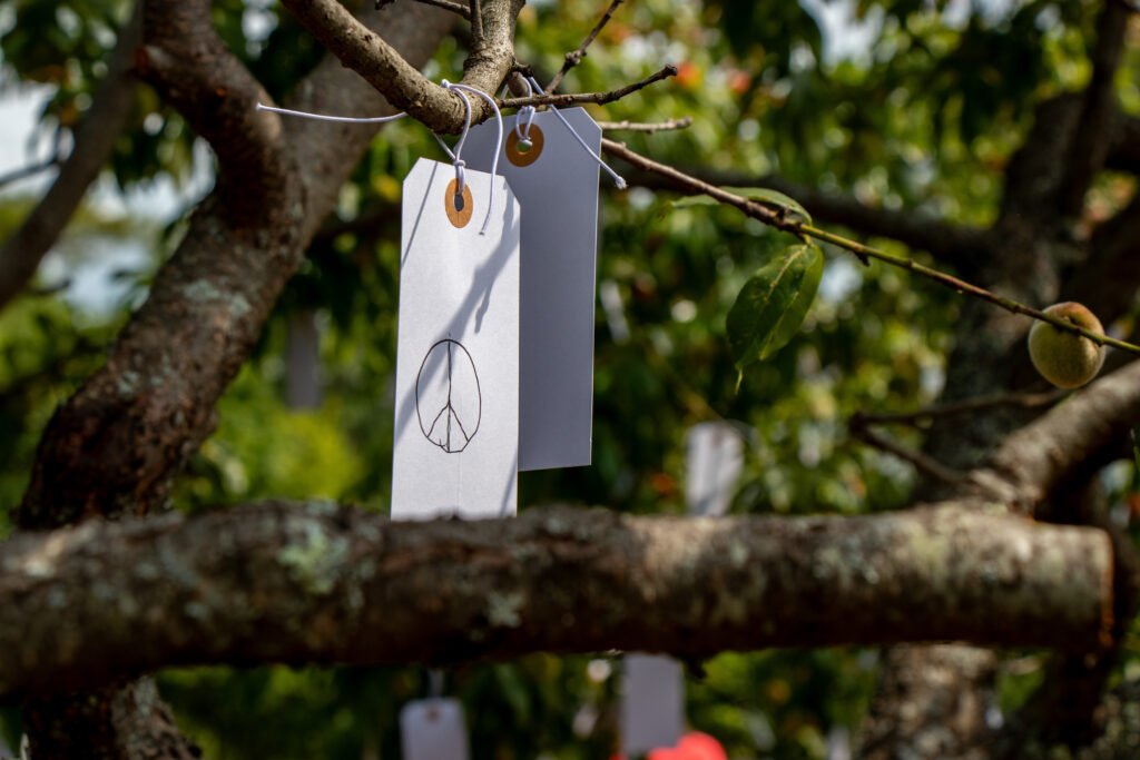 A small white tag hangs from the branches of a tree. On the tag, a peace symbol is written