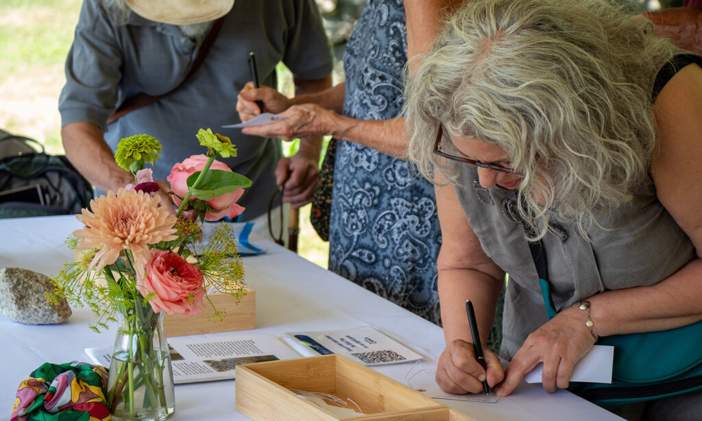 Three people gather around a table adorned with flowers and a white table cloth. They are writing on small pieces of paper.