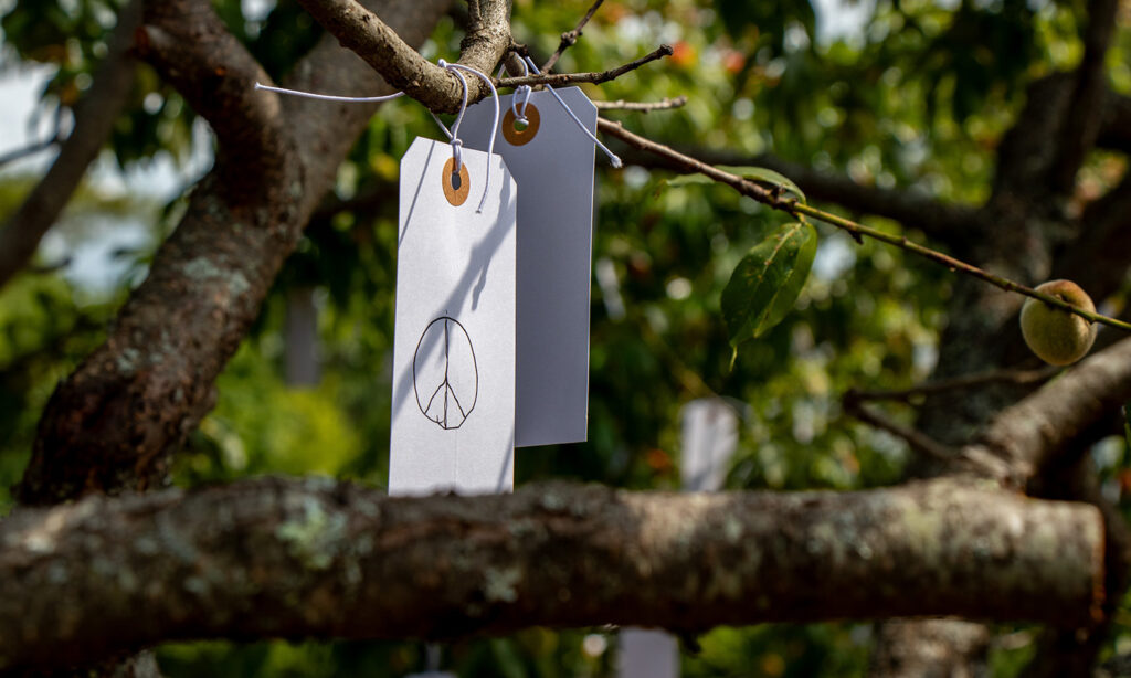 A small white tag hangs from the branches of a tree. On the tag, a peace symbol is written