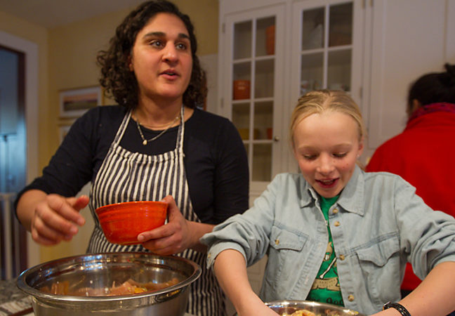 A woman and a little girl stand at a kitchen island and prepare food together