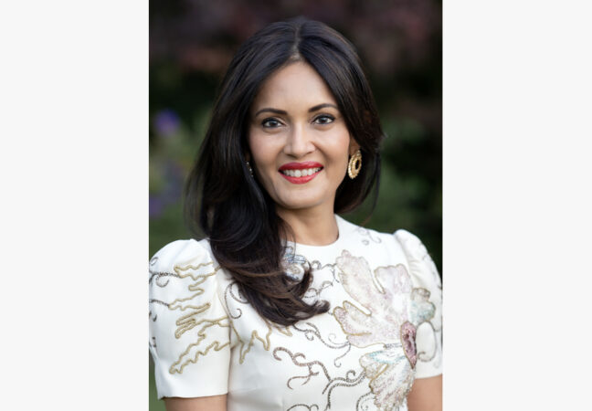 A portrait of Komal Shah. She has long brunette hair and is wearing a intricately stitched white top.