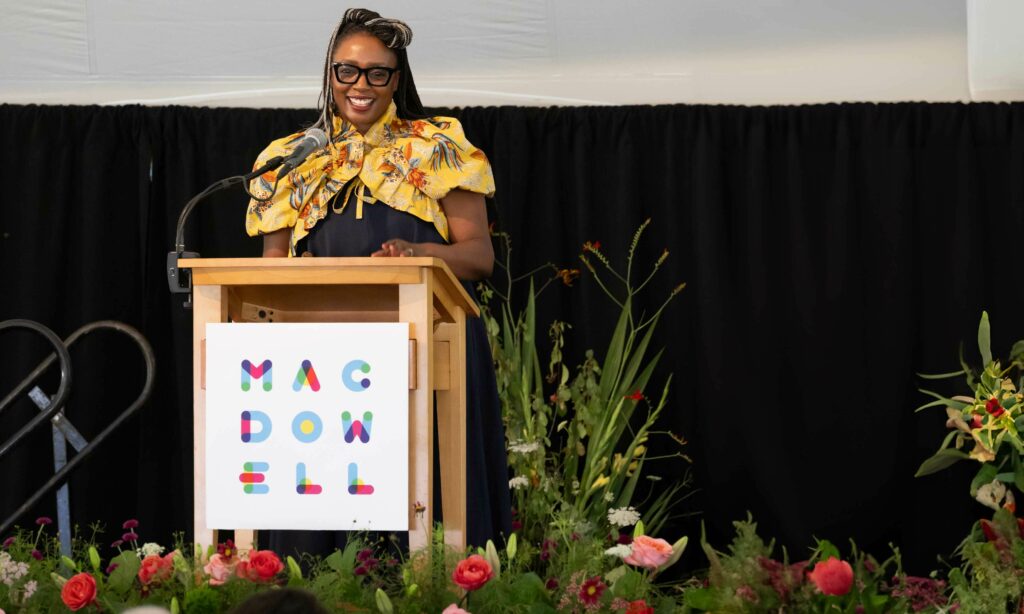 Executive Director of MacDowell Chi Kaitano smiles from behind the lectern at those gathered for Medal Day 2024 during her address.