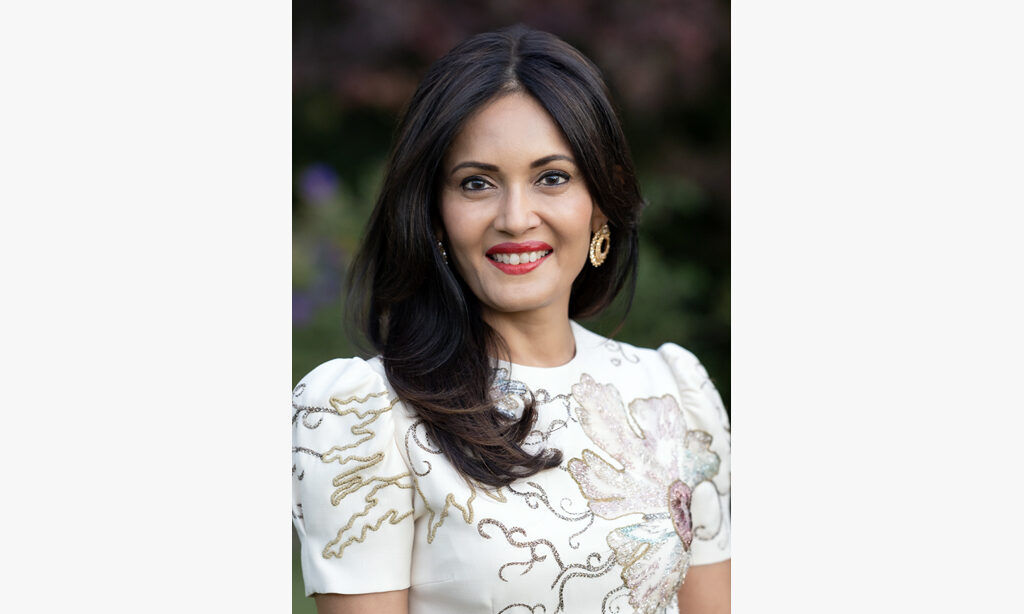 A portrait of Komal Shah. She has long brunette hair and is wearing a intricately stitched white top.