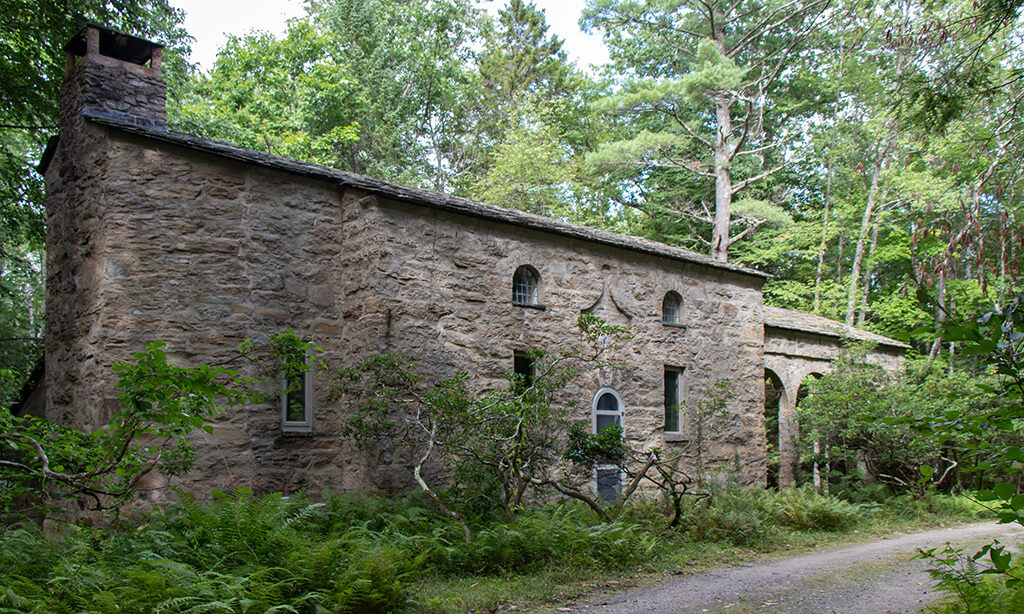 A granite stone building in a dark forest, next to a gravel road.